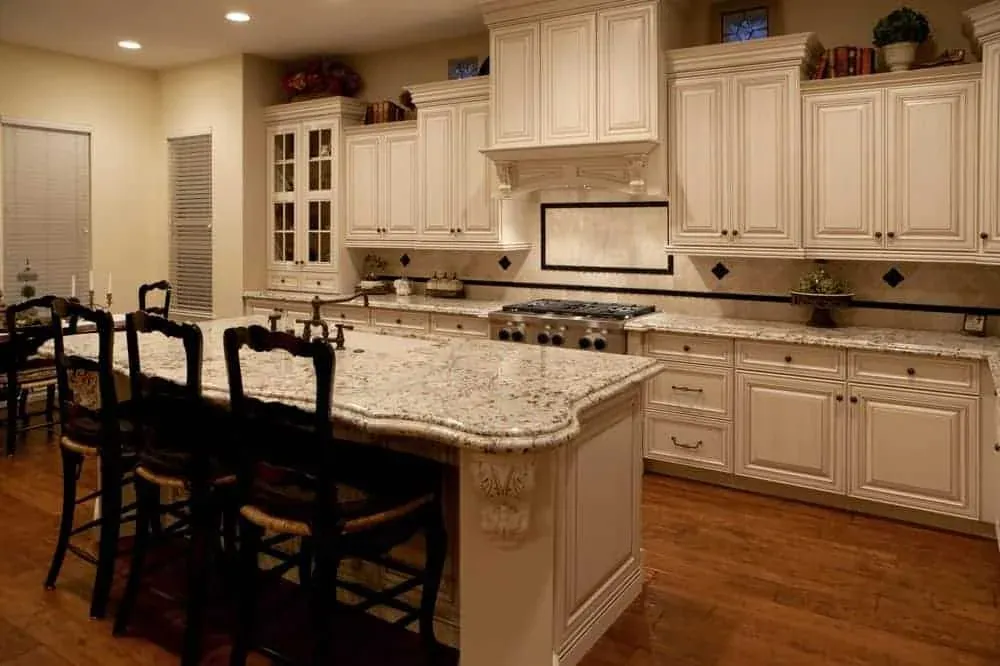Cream kitchen with a granite-top island, dark wood barstools and a patterned area rug on tile flooring