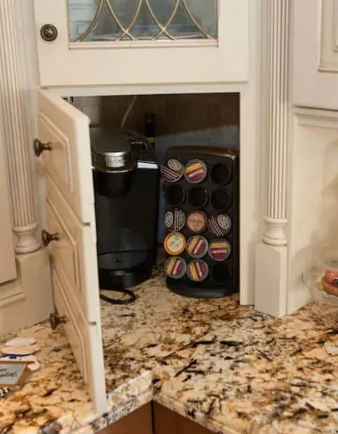 Open appliance garage in cream cabinetry holding a coffee maker and a pod carousel on a granite counter