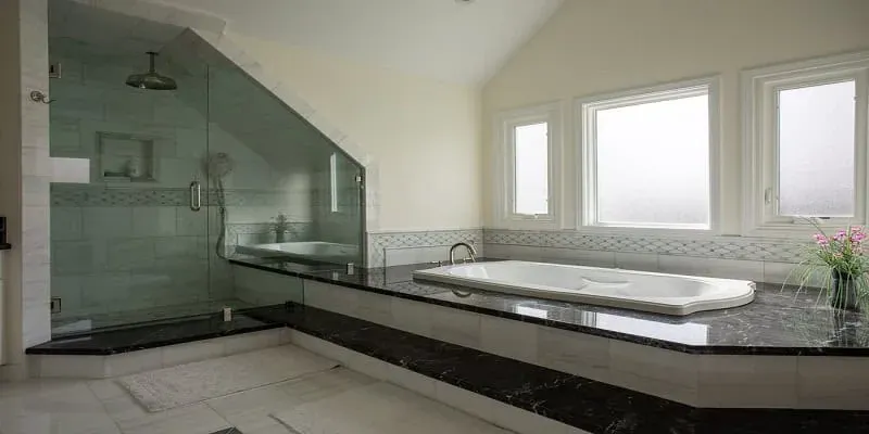 Remodeled bathroom with a glass-enclosed shower beside a built-in soaking tub and dark granite surround under two windows