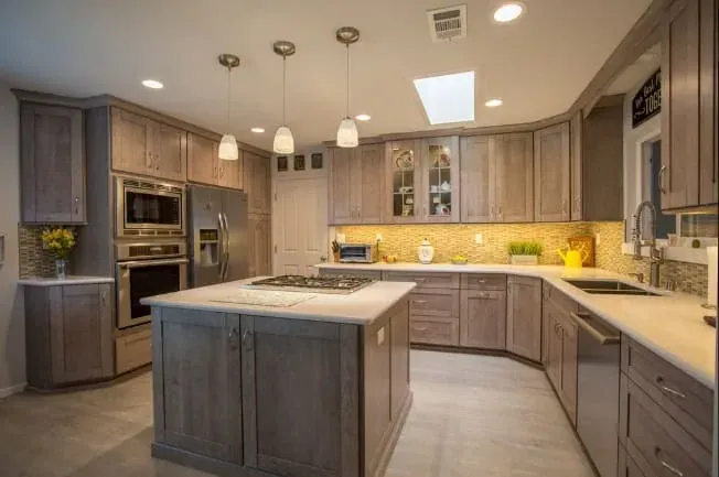 gray wood-tone kitchen with center island cooktop, pendant lighting and stainless refrigerator