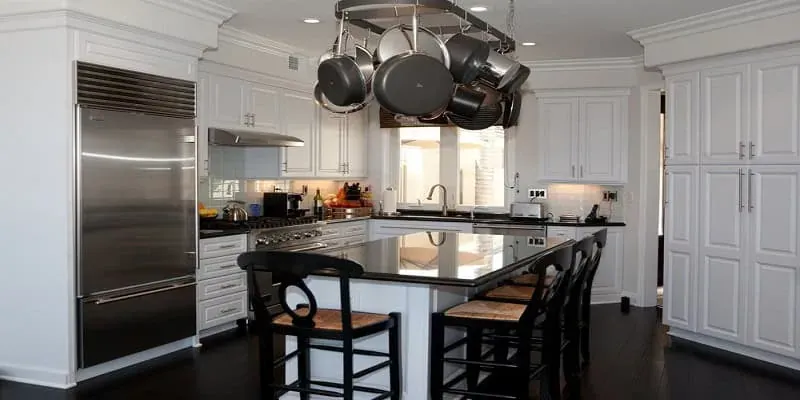 White kitchen with a black granite island, a hanging pot rack overhead and dark wood barstools