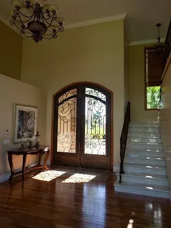 Entryway with a wrought-iron double door, a staircase, a wood console table and a hanging chandelier