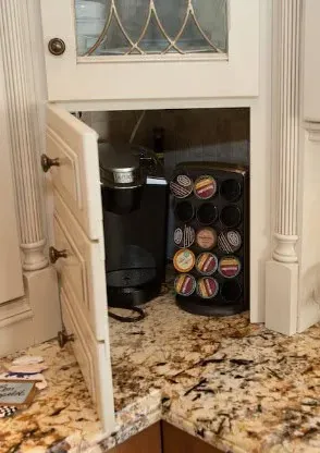 Open white cabinet door revealing a built-in coffee maker and a k-cup pod storage rack