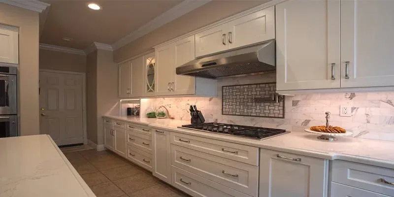 White shaker cabinets with a marble-look backsplash, stainless range hood and gas cooktop