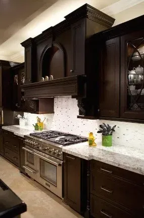 dark espresso cabinets with white marble backsplash tile, stainless range and beige tile flooring