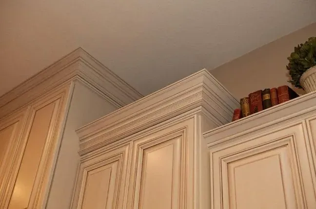 Upper corner of cream kitchen cabinets with crown molding, a book stack and a small potted plant