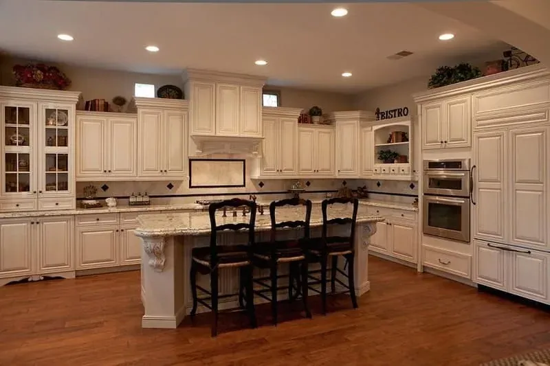 Cream cabinet kitchen with a dark wood island, granite countertops, black bar stools and glass-front upper cabinets