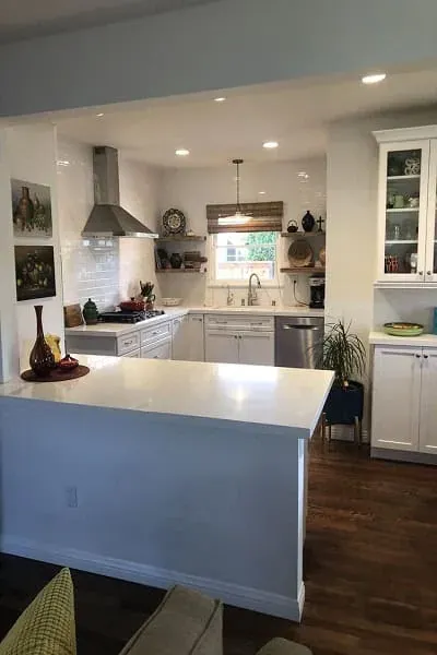 Open white kitchen with a stainless range hood, subway tile backsplash and a peninsula counter