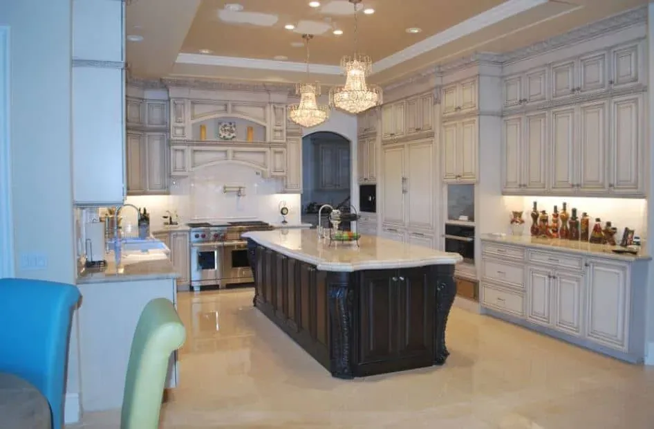 ornate cream kitchen with dark wood carved-leg island, crystal chandeliers and stainless range