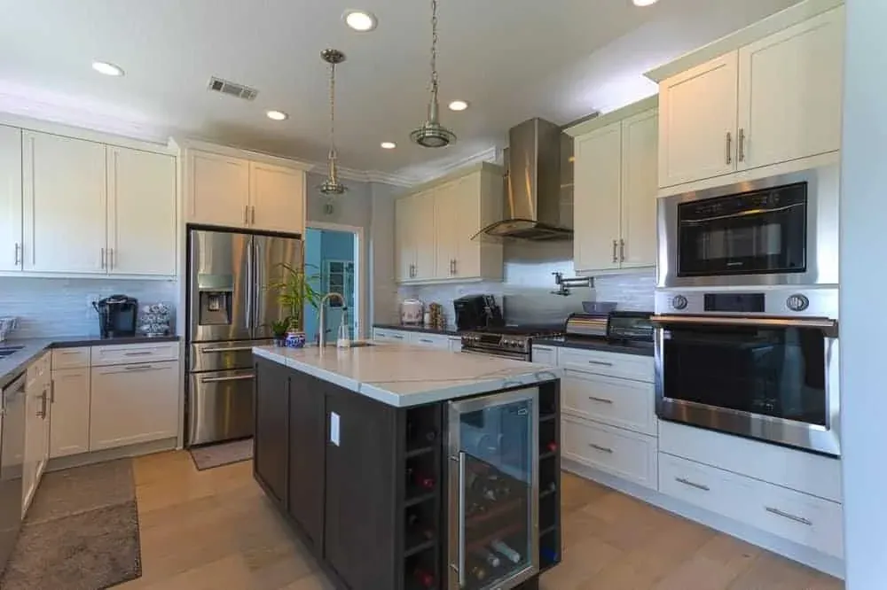 White kitchen with a dark island holding a wine cooler, stainless appliances beyond