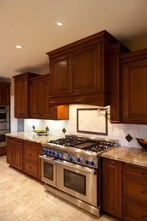 Dark wood cabinets frame a stainless gas range beneath a tiled backsplash medallion