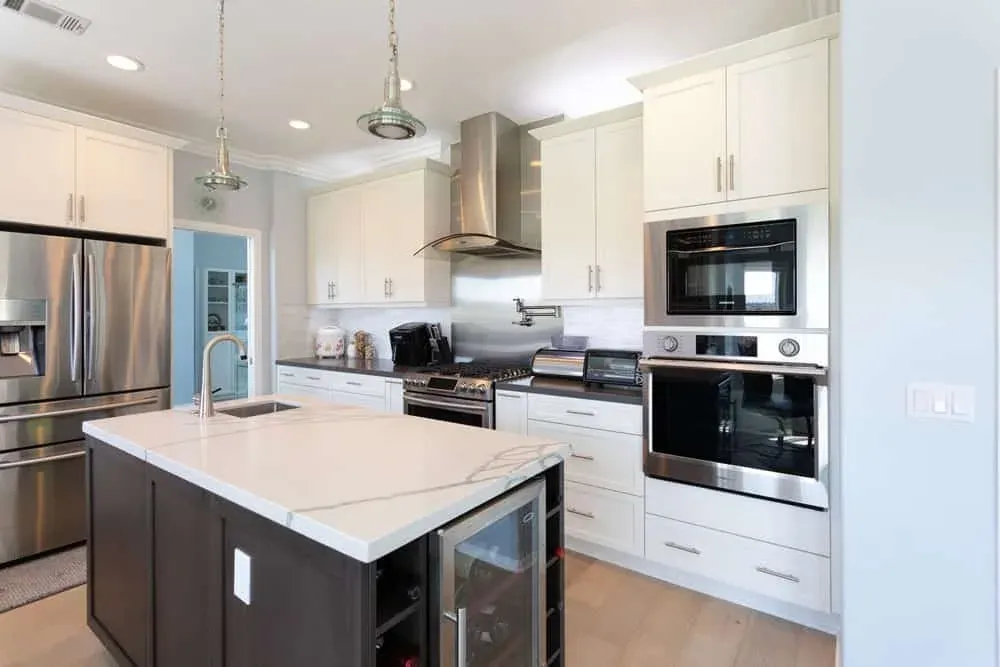 Mission Viejo kitchen with white cabinets, a stainless hood, a dark island and a wine cooler