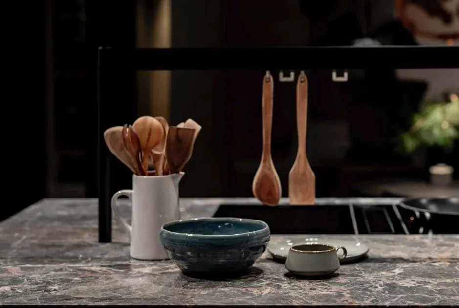 dark stone island countertop with a blue ceramic bowl, small dish and wooden utensils hanging from a black rail