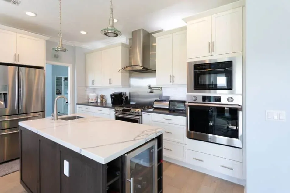 White cabinet kitchen with stainless appliances, dark island cabinetry and a light stone-look countertop