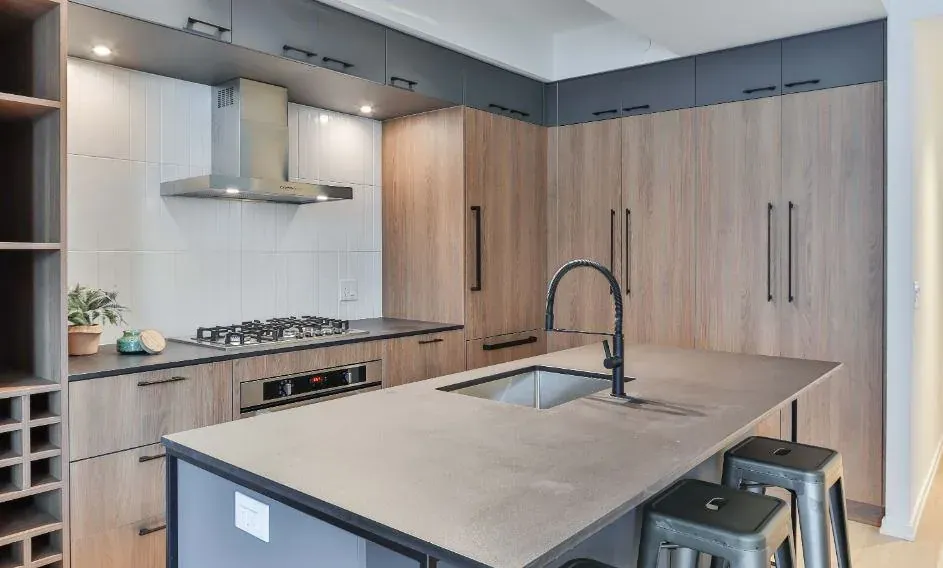 Modern kitchen with wood-grain cabinets, a long concrete-look island counter and black metal bar stools