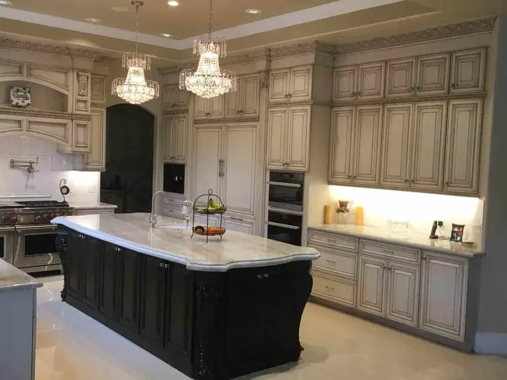Glazed cabinetry run to the ceiling around a dark island with crystal chandeliers