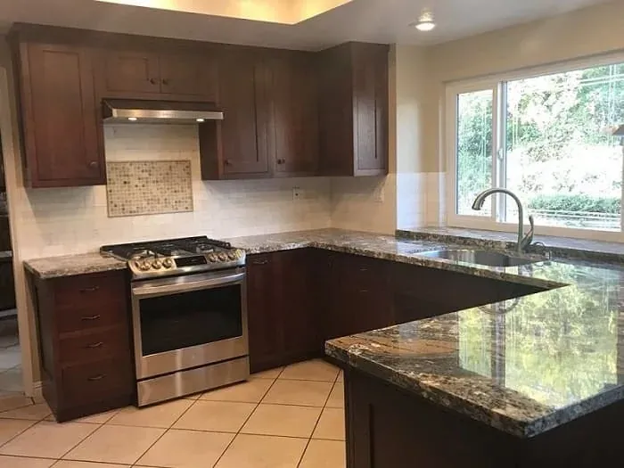dark wood cabinets with granite countertops, gas range and tile backsplash near window