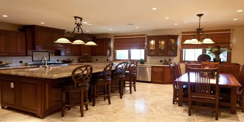 long wood island with granite countertop and round-back bar stools beside a wood dining table
