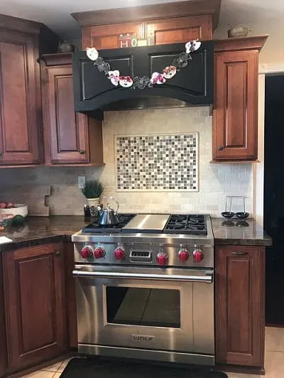 Stainless range with red control knobs beneath a mosaic tile backsplash flanked by cherry wood cabinets