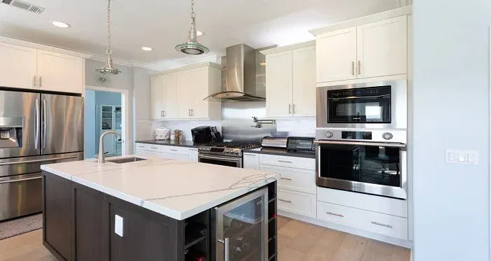 White shaker kitchen with a dark island, a quartz top, a wine fridge and a stainless steel chimney hood