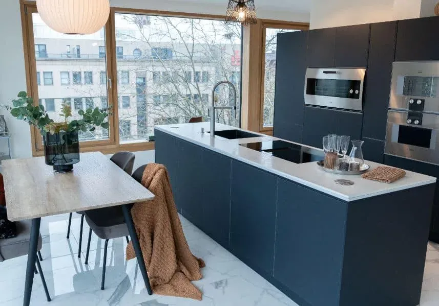 Dark navy modern kitchen with a waterfall island, wood dining table and large windows behind