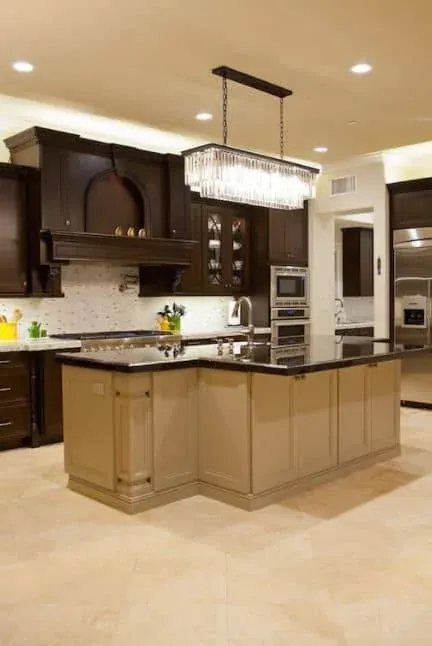 Espresso cabinetry with black granite counters and a light tan island beneath a crystal chandelier
