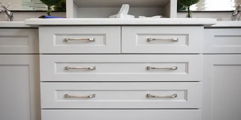 white bathroom vanity with brushed nickel pulls, drawer bank and mirror reflections at the counter edge