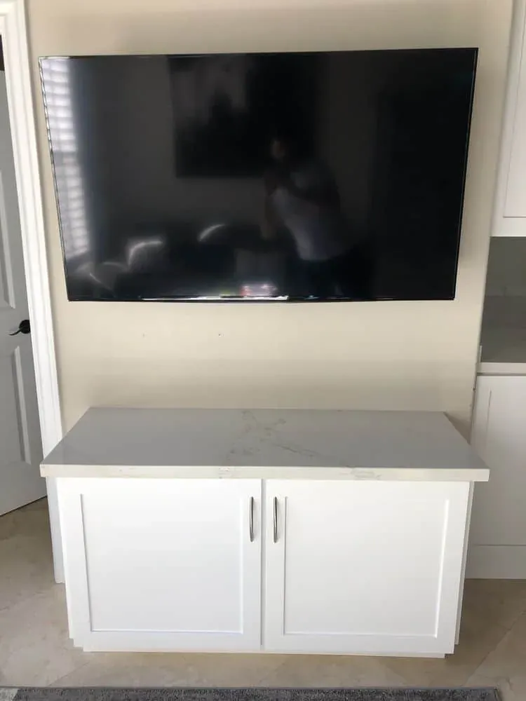 Wall-mounted flat-screen television above a white cabinet with a light stone-look countertop in a living room