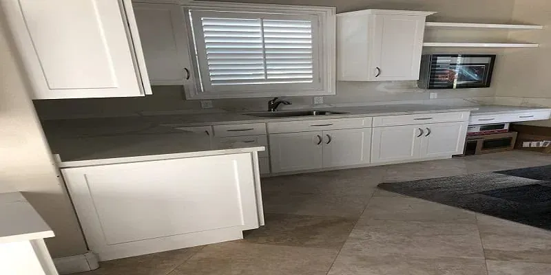 White shaker cabinets with a gray countertop, a window with blinds and floating shelves above tile flooring