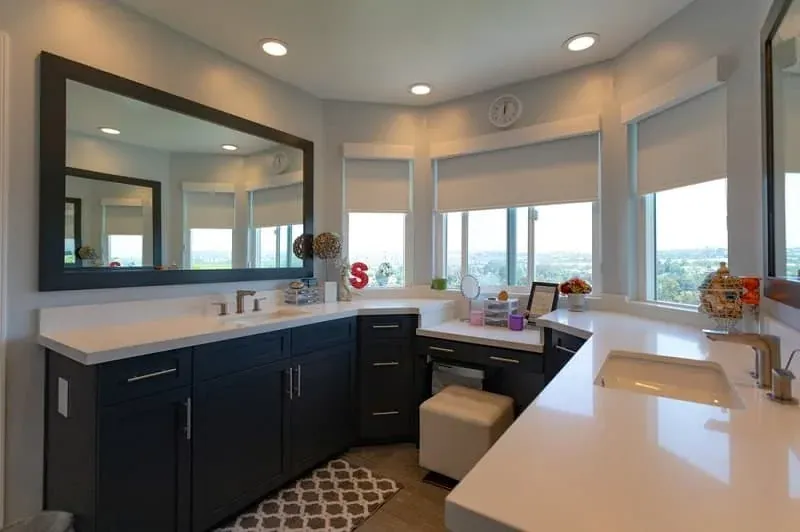 Dark cabinet bathroom vanity with white quartz countertop, a wall mirror and roller shades over view windows
