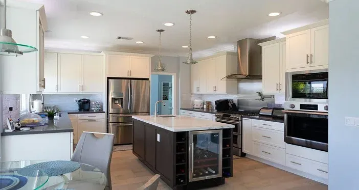 white kitchen with stainless steel refrigerator, a dark wood island with white quartz countertop and built-in wine cooler