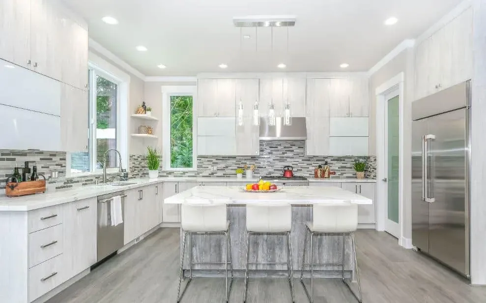 White kitchen with a mosaic tile backsplash and an island with three bar stools