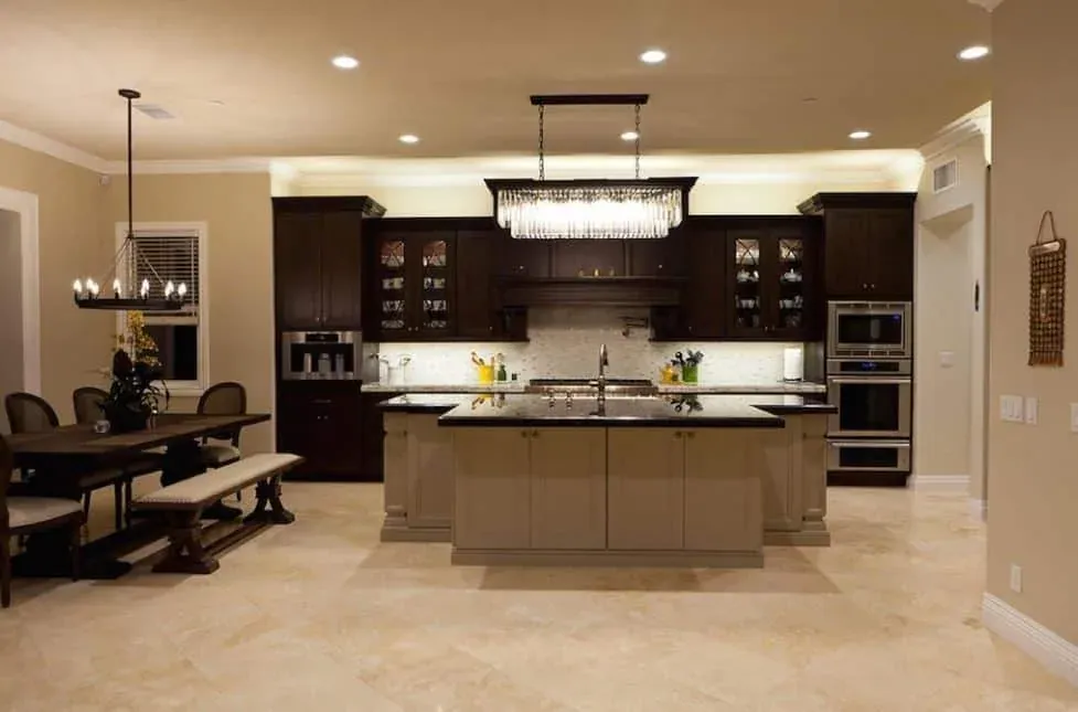Espresso kitchen with a pale island and a linear chandelier over a stone floor