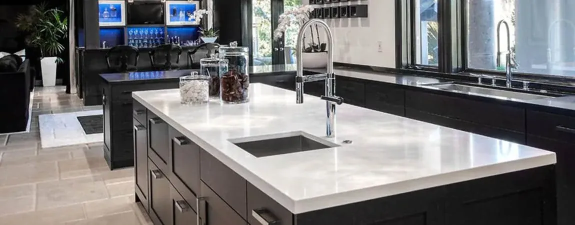 White quartz island with an undermount sink facing dark cabinetry and a window run