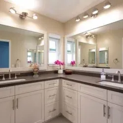Long white bathroom vanity with a dark stone top, two undermount sinks and wide wall mirrors