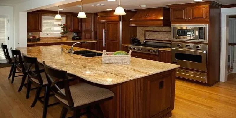 Medium wood cabinetry with a granite-topped island seating area, stainless double oven and microwave