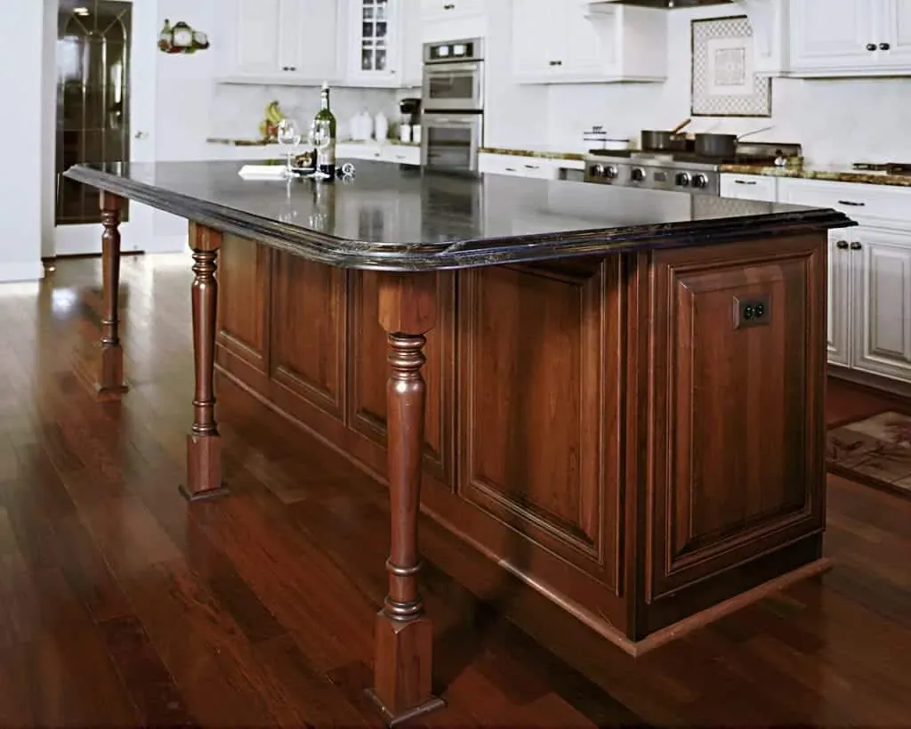 Cherry kitchen island with a turned post leg and a black granite top on a wood floor