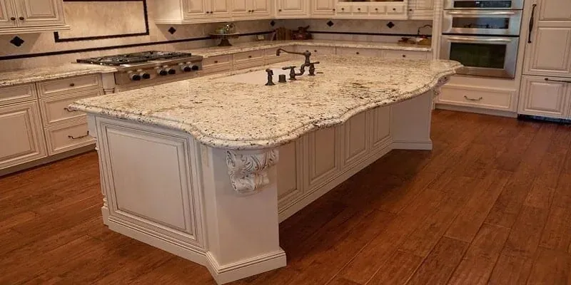 Cream kitchen island with a carved corbel and a light granite countertop above dark wood flooring