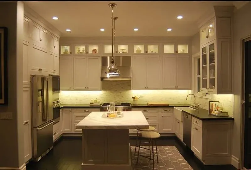 White kitchen with a dark wood island, stainless refrigerator column and woven bar stools on dark flooring