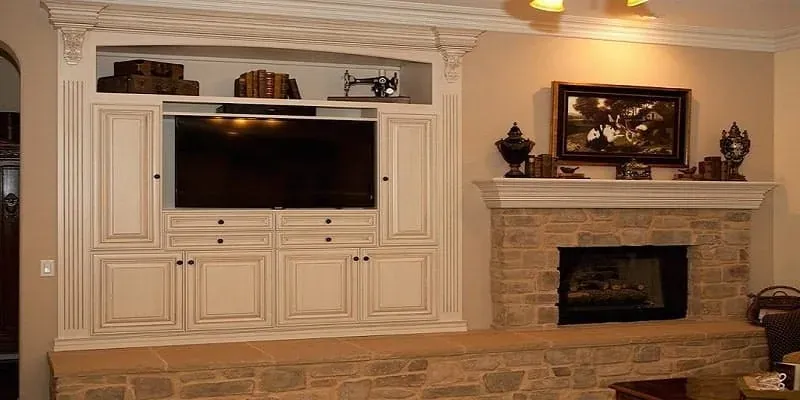 White built-in entertainment cabinet with a television niche and bookshelf beside a stone fireplace