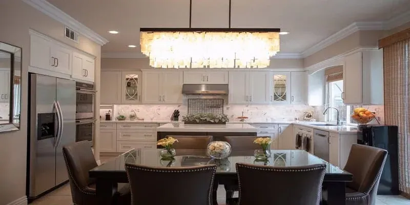 White kitchen open to a dining area with a rectangular crystal chandelier over a dark wood table