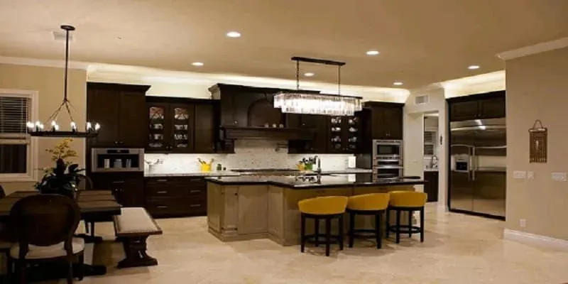 dark wood kitchen with black-topped island, yellow bar stools and crystal linear chandelier