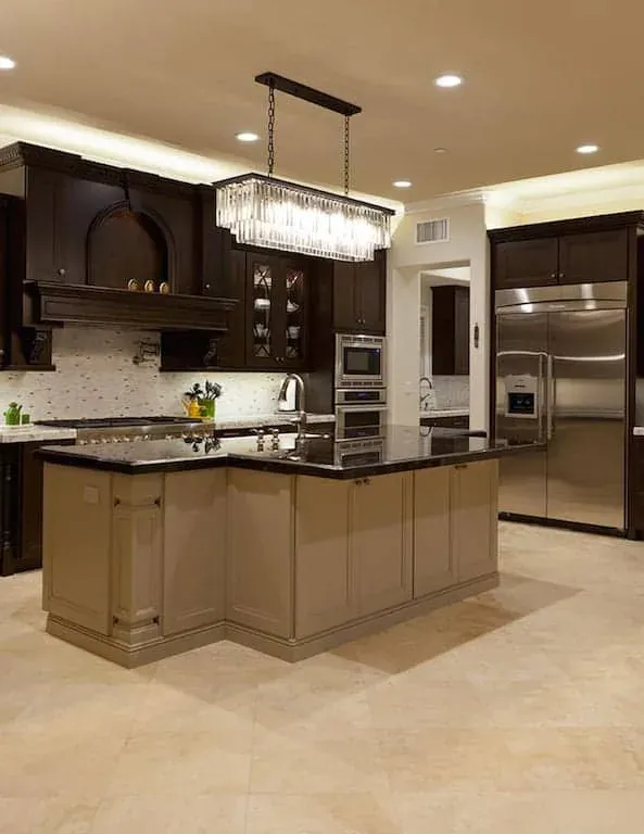 Dark kitchen with a linear chandelier, island and stainless refrigerator