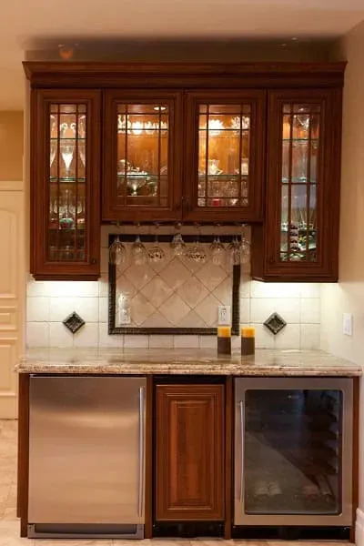 glass-front upper cabinets holding stemware and glassware above a stainless beverage fridge and wine cooler