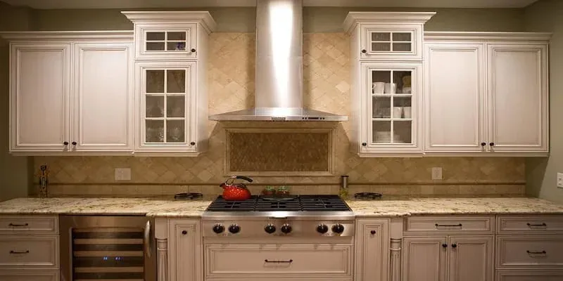 Cream cabinets with glass-front uppers either side of a stainless chimney hood