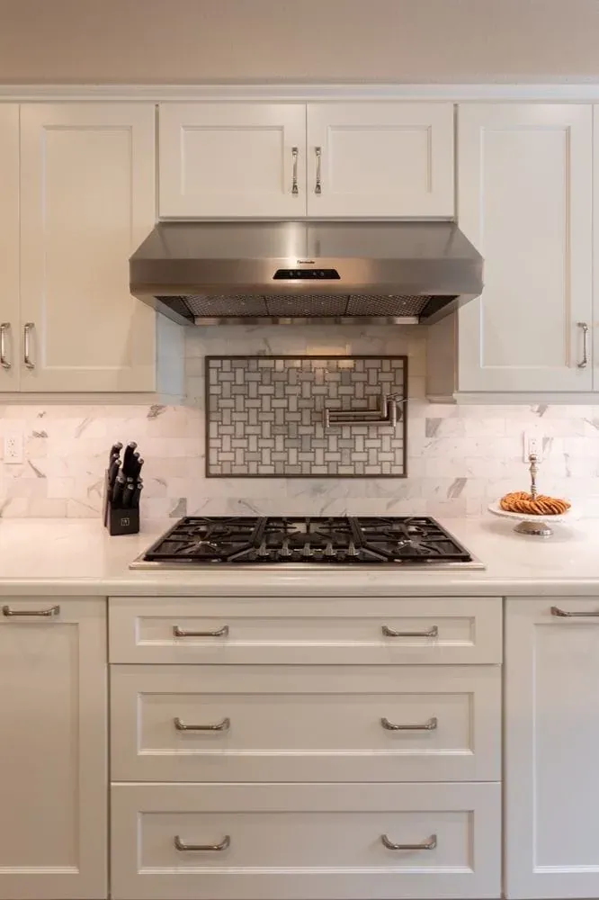 White cabinets around a stainless hood with a tile mural above the cooktop