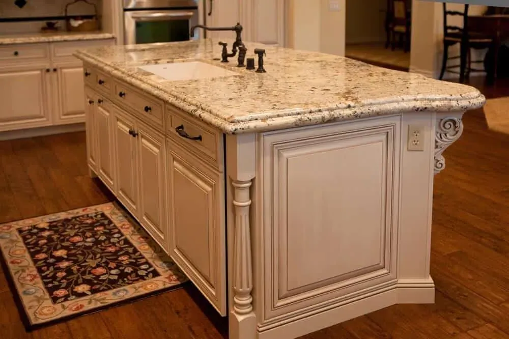 Cream island with carved corbels and a granite top on a wood floor