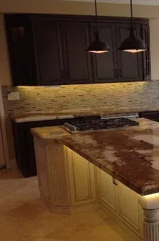Dark wall cabinets over a mosaic tile backsplash and a granite-topped cream island lit along its base