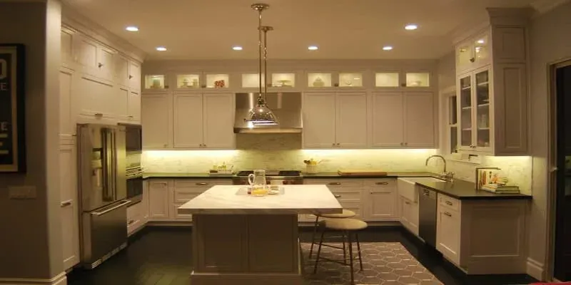 White kitchen with a marble-look island, glass-front upper cabinets and dark hardwood flooring