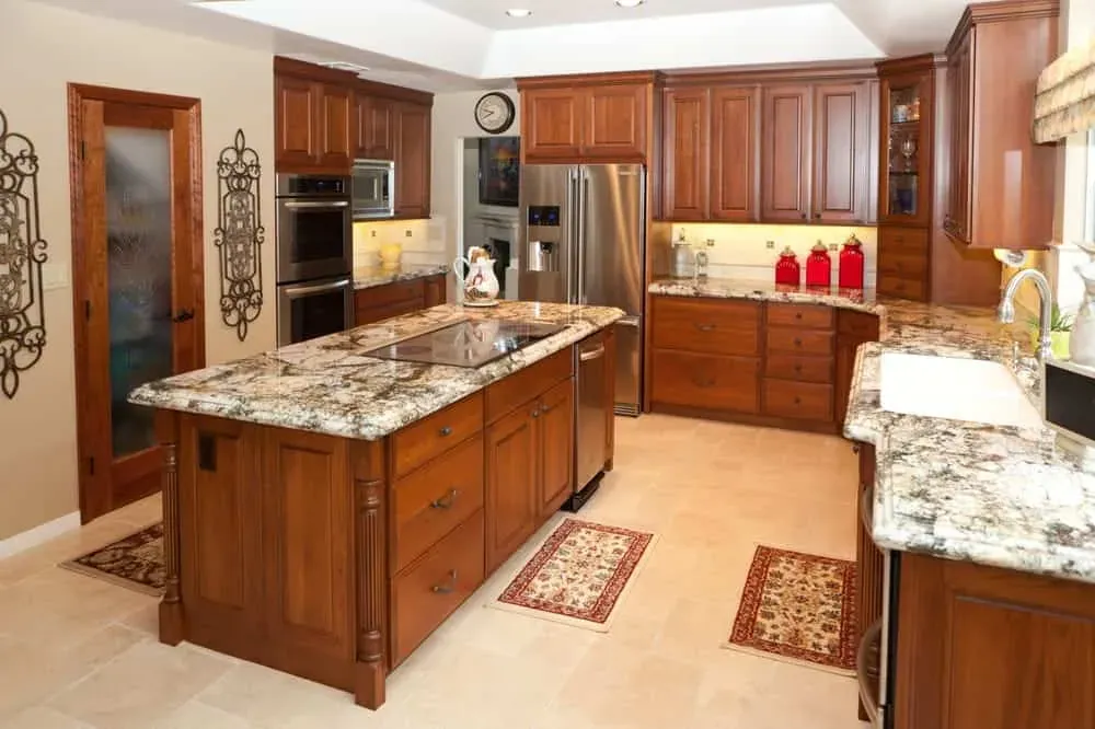 Cherry kitchen with a granite island, stainless appliances and a travertine floor with rugs